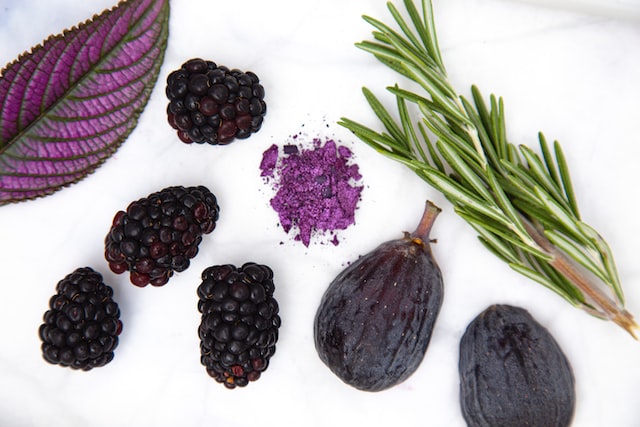 Purple leaf, black raspberries, purple powder, fig and thymes on a table